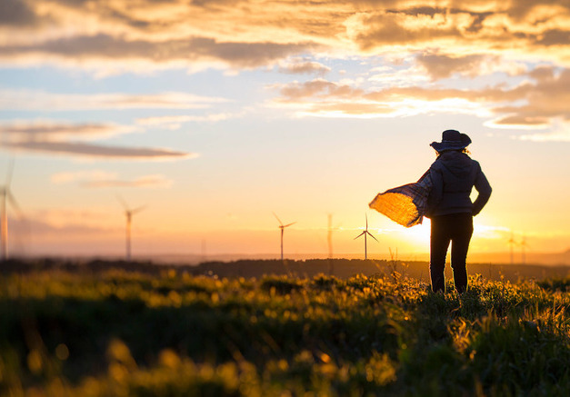 Farmer watching field at sunset with windmills in the background